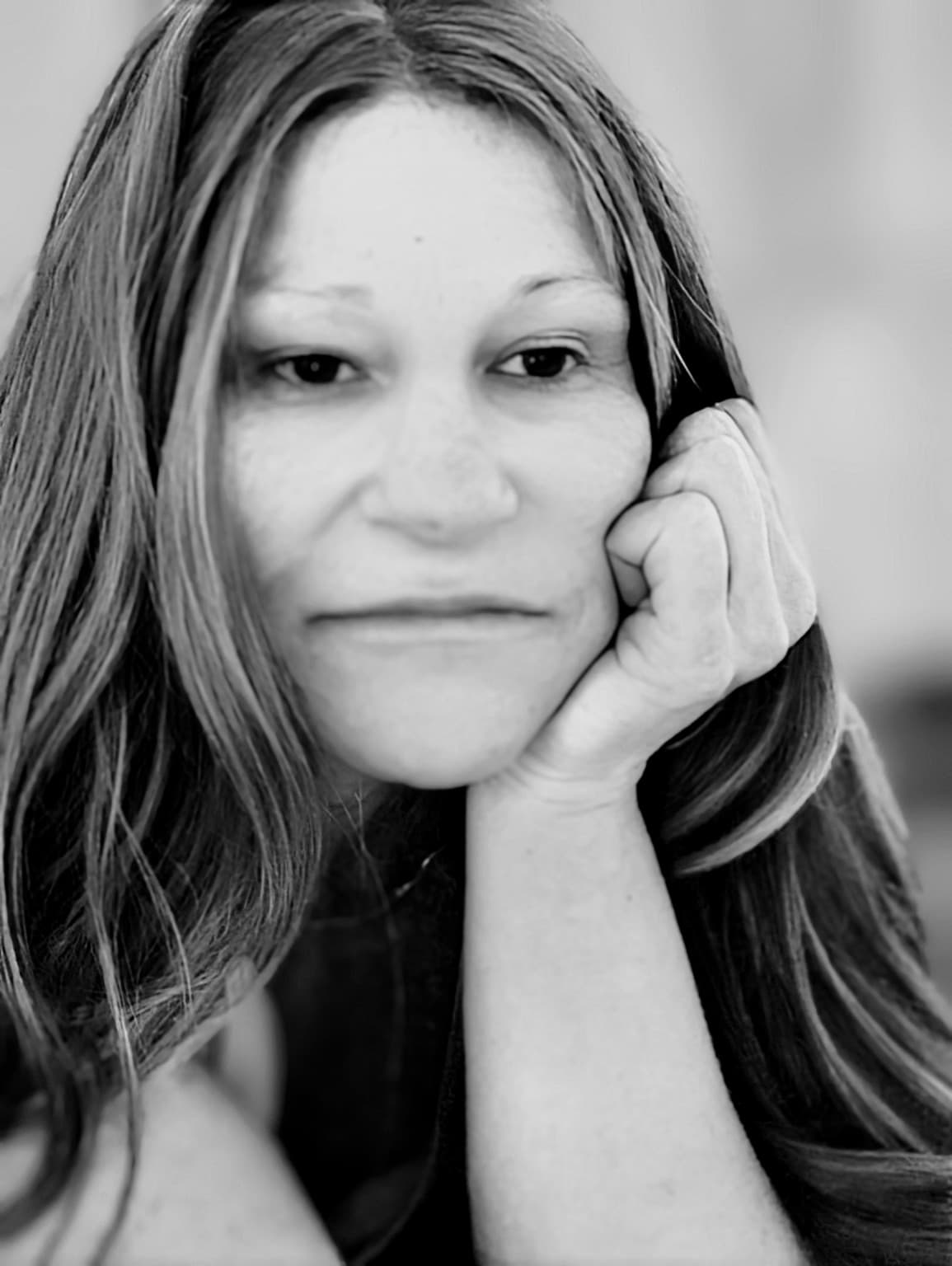 Black and white portrait of a woman with long hair resting her chin on hand.